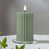 Zöld Stripe LED gyertya dekor pohárban elhelyezve, meleg fényben világítva, zöld növényi elemekkel körülvéve, meghitt beltéri hangulatban.